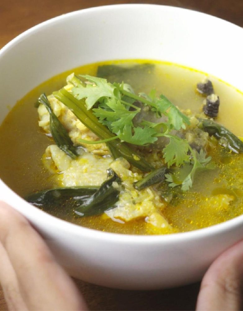 Kyat thout san, a golden hot and sour chicken soup with culantro, in a white bowl