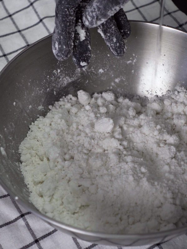 Water being poured slowly into the flour while mixing by hand