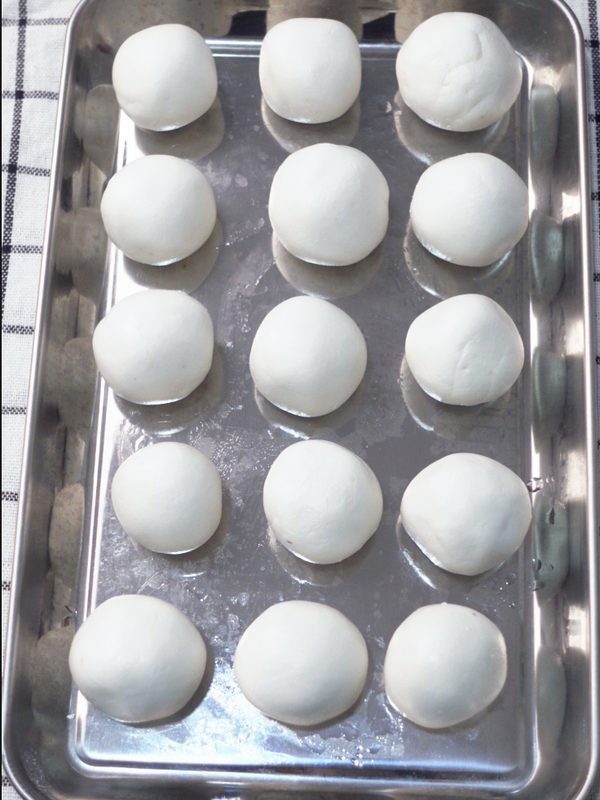Fifteen uncooked rice balls lined up on a steel tray